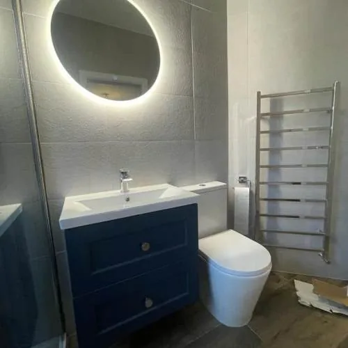 Bathroom with round LED mirror, navy vanity unit and wood-effect floor